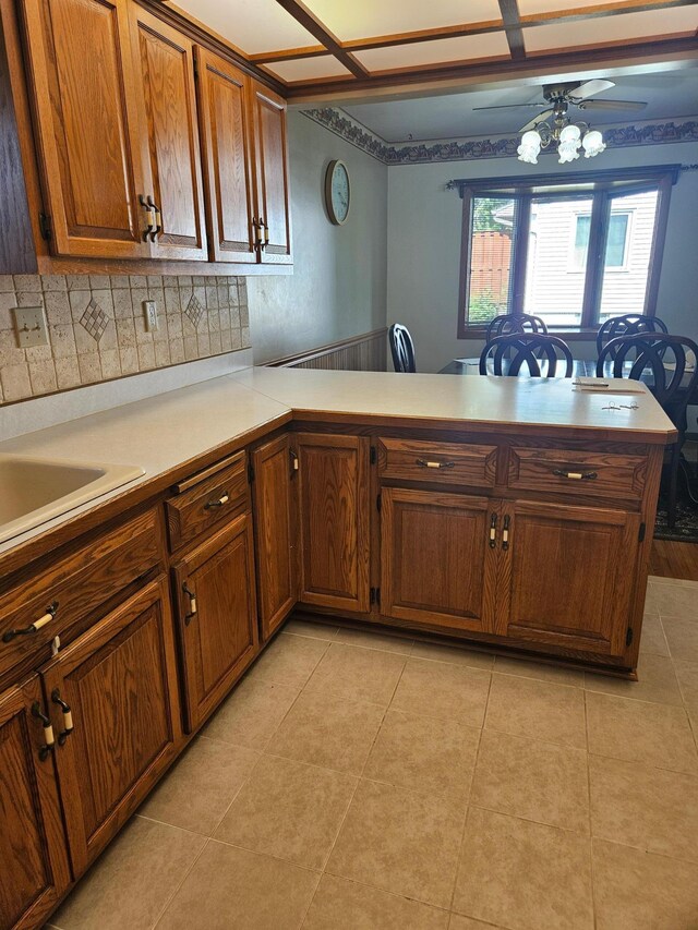 5306 Boulder Ln, Brooklyn Center, MN 55429 - kitchen featuring light countertops, a peninsula, brown cabinets, a wainscoted wall, and tasteful backsplash