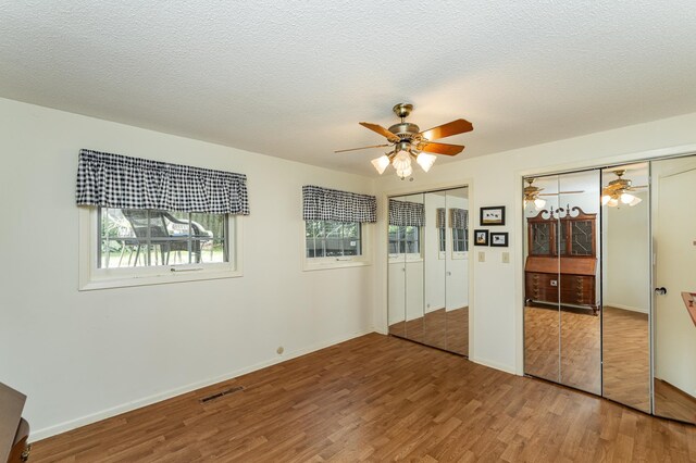 625 Folwell Ln SW, Rochester, MN 55902 - unfurnished bedroom with two closets, wood finished floors, multiple windows, a ceiling fan, and a textured ceiling
