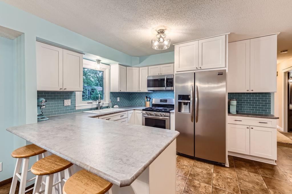 13107 Van Buren St NE, Blaine, MN 55434 - kitchen featuring appliances with stainless steel finishes, a peninsula, white cabinetry, and a textured ceiling