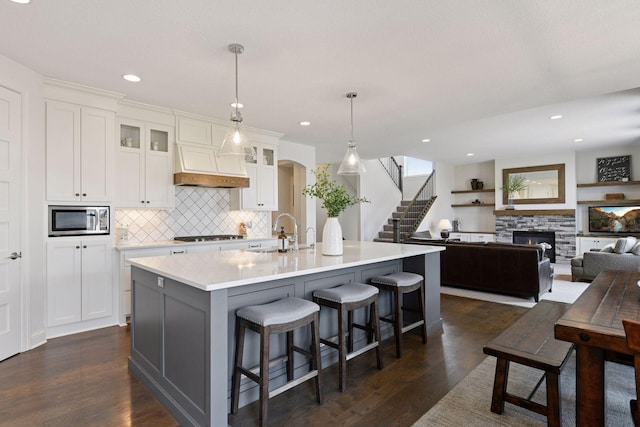 6333 Yuma Ln N, Maple Grove, MN 55311 - kitchen with stainless steel microwave, backsplash, white cabinetry, a kitchen island with sink, and dark wood-style flooring