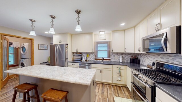 216 1st St, Kiester, MN 56051 - kitchen with appliances with stainless steel finishes, stacked washer and clothes dryer, light wood-type flooring, tasteful backsplash, and a breakfast bar