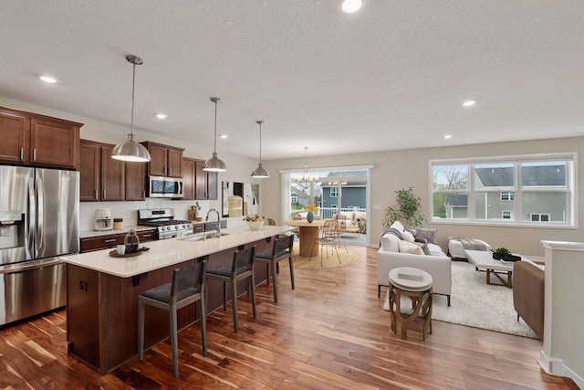 5743 Meridian Way NE, Prior Lake, MN 55372 - kitchen featuring stainless steel appliances, dark wood finished floors, a kitchen bar, a kitchen island with sink, and light countertops