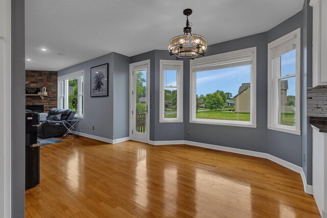 1302 Grizzly Ln, Sartell, MN 56377 - unfurnished dining area with light wood-style flooring, a chandelier, a fireplace, recessed lighting, and a textured ceiling