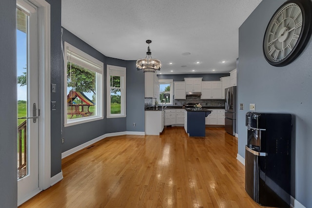 1302 Grizzly Ln, Sartell, MN 56377 - kitchen with dark countertops, decorative backsplash, a center island, white cabinets, and light wood finished floors