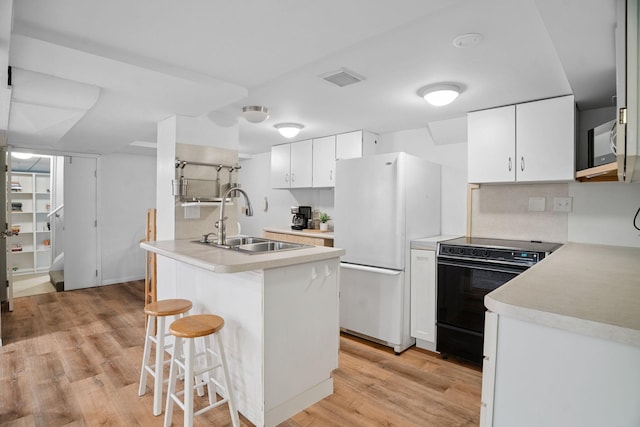 1511 Branston St, Saint Paul, MN 55108 - kitchen featuring black range with electric stovetop, freestanding refrigerator, light wood-style floors, a kitchen bar, and light countertops