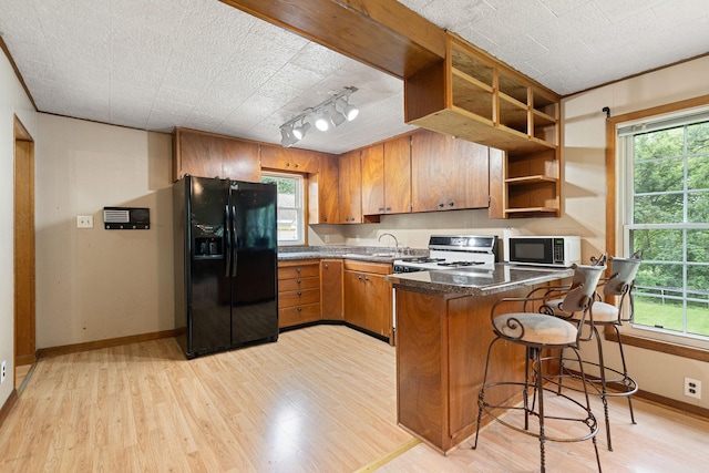 208 12th St SE, Austin, MN 55912 - kitchen with black fridge, white gas range oven, a peninsula, brown cabinetry, and light wood-style floors