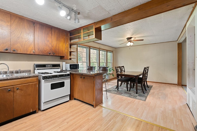 208 12th St SE, Austin, MN 55912 - kitchen with white gas range oven, track lighting, light wood finished floors, brown cabinetry, and dark countertops