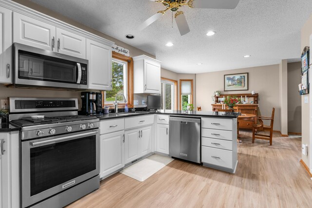 330 11th St NW, Byron, MN 55920 - kitchen with stainless steel appliances, dark countertops, a peninsula, a ceiling fan, and white cabinetry