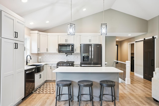 1623 Otter Way, New Richmond, WI 54017 - kitchen featuring appliances with stainless steel finishes, lofted ceiling, light wood-type flooring, a barn door, and light countertops