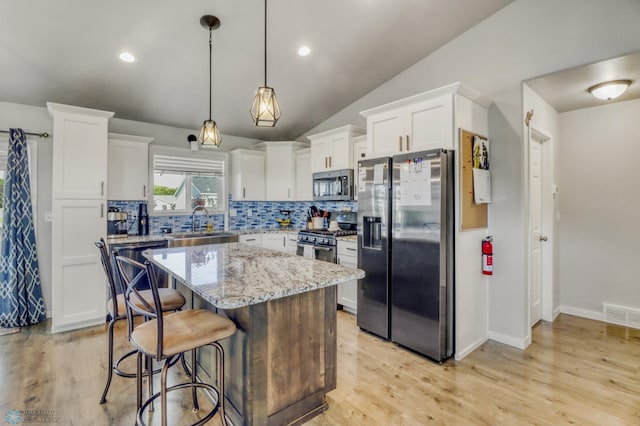1334 6th St NW, Fargo, ND 58078 - kitchen featuring stainless steel appliances, decorative backsplash, white cabinets, a kitchen bar, and a center island