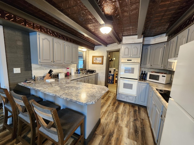 207 Mill Rd, Park Rapids, MN 56470 - kitchen featuring white appliances, a peninsula, dark wood-type flooring, an ornate ceiling, and a breakfast bar