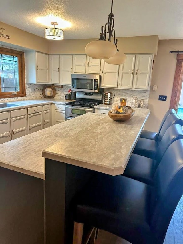 902 6th Ave SE, Pipestone, MN 56164 - kitchen featuring appliances with stainless steel finishes, white cabinets, light countertops, a breakfast bar area, and tasteful backsplash
