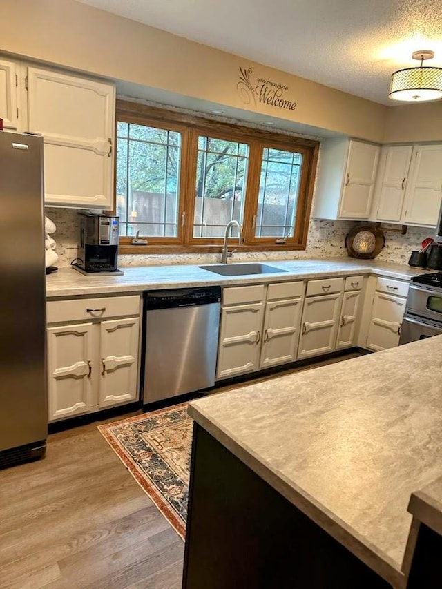 902 6th Ave SE, Pipestone, MN 56164 - kitchen with appliances with stainless steel finishes, light wood-style flooring, white cabinetry, light countertops, and decorative backsplash