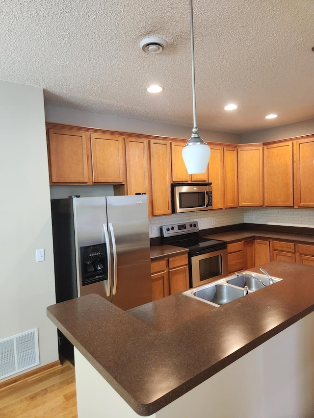 703 10th St S, Buffalo, MN 55313 - kitchen with stainless steel appliances, dark countertops, light wood-type flooring, tasteful backsplash, and a textured ceiling