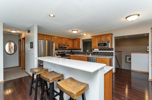 3714 8th St NW, Rochester, MN 55901 - kitchen with appliances with stainless steel finishes, under cabinet range hood, brown cabinetry, dark wood-type flooring, and light countertops