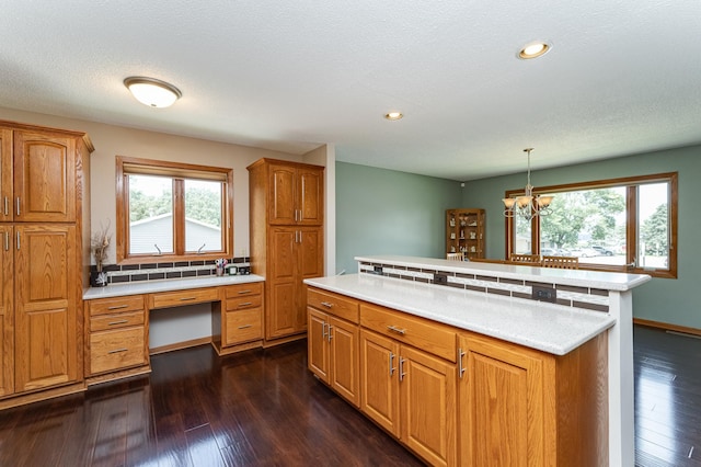 3714 8th St NW, Rochester, MN 55901 - kitchen featuring light countertops, dark wood finished floors, a center island, built in desk, and brown cabinetry