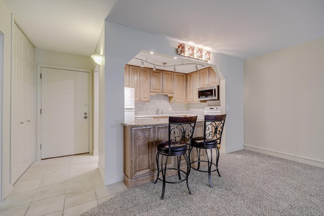 10521 Cedar Lake Rd Unit 208, Minnetonka, MN 55305 - kitchen featuring stainless steel microwave, a breakfast bar, tasteful backsplash, freestanding refrigerator, and light tile patterned floors