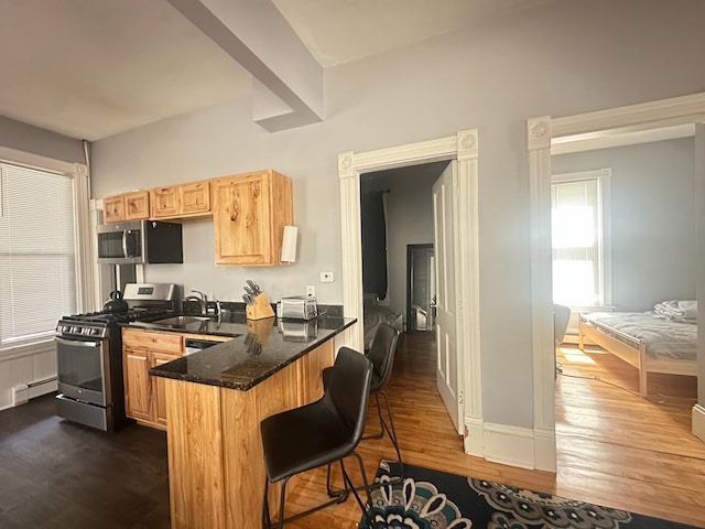 713 2nd St NE, Minneapolis, MN 55413 - kitchen featuring appliances with stainless steel finishes, dark wood finished floors, dark stone countertops, a peninsula, and a breakfast bar