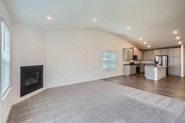 1221 136th St W, Rosemount, MN 55068 - unfurnished living room featuring healthy amount of natural light, vaulted ceiling, dark carpet, recessed lighting, and a glass covered fireplace