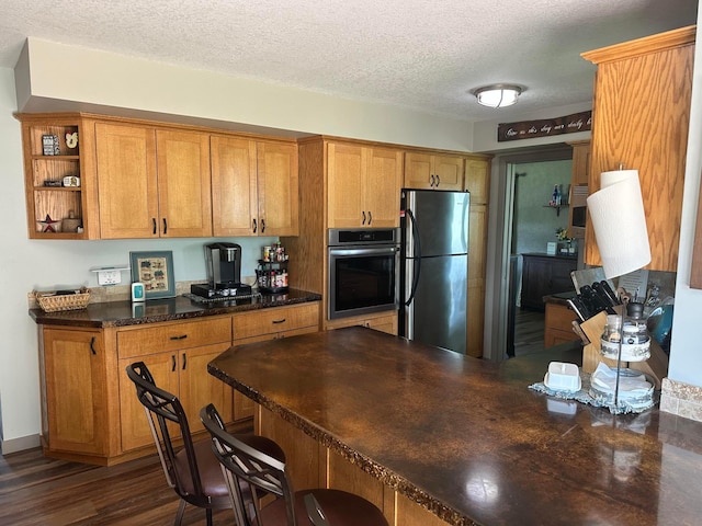 515 2nd St SW, New Richland, MN 56072 - kitchen with stainless steel oven, freestanding refrigerator, a textured ceiling, a breakfast bar, and brown cabinets