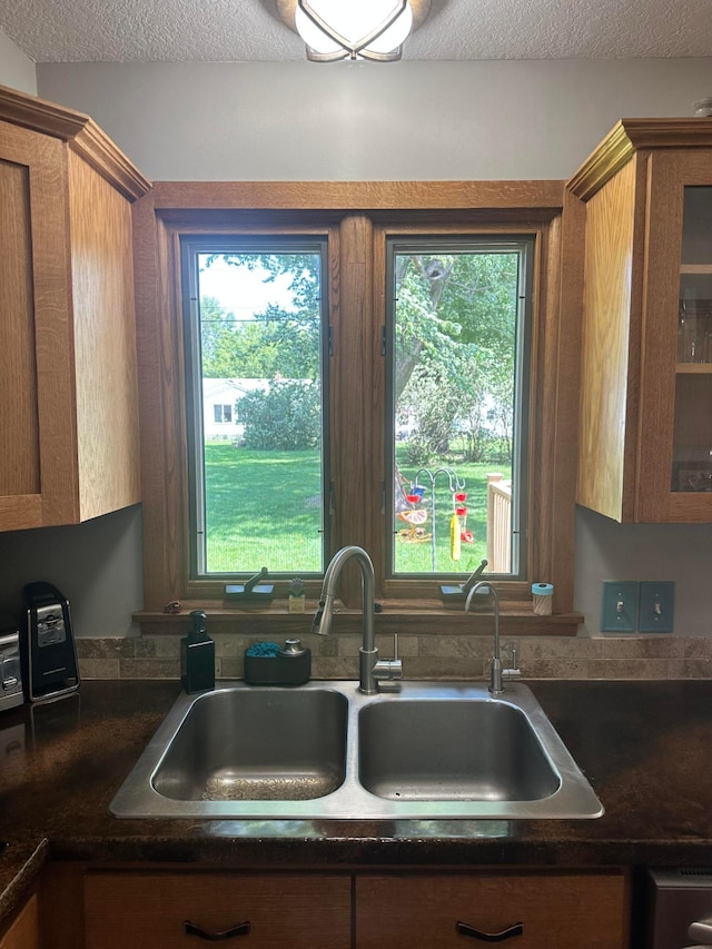 515 2nd St SW, New Richland, MN 56072 - kitchen featuring brown cabinetry, dark countertops, a textured ceiling, and glass insert cabinets