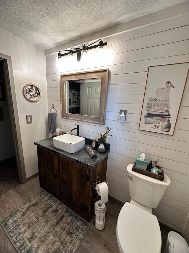 515 2nd St SW, New Richland, MN 56072 - half bath featuring wood finished floors, a textured ceiling, vanity, and wooden walls