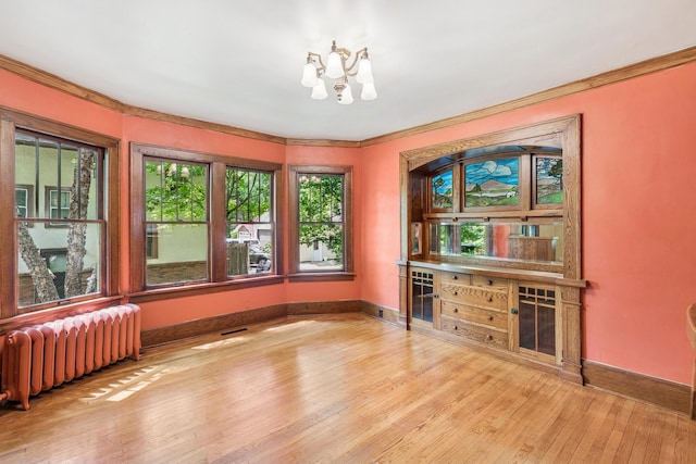 713 4th St E, Northfield, MN 55057 - empty room with radiator heating unit, ornamental molding, hardwood / wood-style flooring, a chandelier, and a dry bar