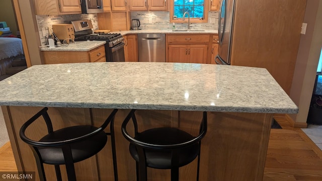 21021 Fresno St NW, Elk River, MN 55330 - kitchen featuring appliances with stainless steel finishes, a breakfast bar, decorative backsplash, and light wood-style floors