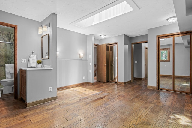 6230 Elm Ridge Cir, Corcoran, MN 55340 - unfurnished bedroom featuring two closets, a skylight, hardwood / wood-style floors, connected bathroom, and wainscoting