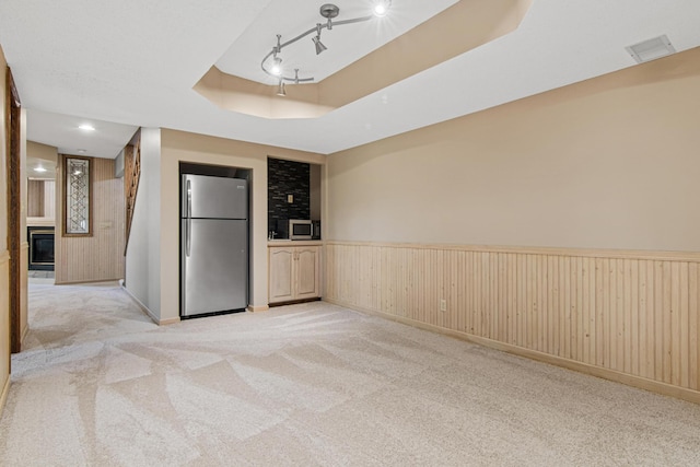 6230 Elm Ridge Cir, Corcoran, MN 55340 - empty room featuring a tray ceiling, light colored carpet, a wainscoted wall, wood walls, and a glass covered fireplace