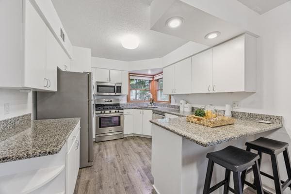 3916 Thomas Ave S, Minneapolis, MN 55410 - kitchen featuring stainless steel appliances, a peninsula, white cabinetry, light wood-style floors, and stone counters
