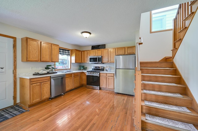 927 Charles Ave, Saint Paul, MN 55104 - kitchen featuring appliances with stainless steel finishes, light countertops, light wood finished floors, a textured ceiling, and brown cabinetry
