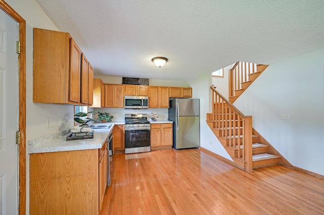 927 Charles Ave, Saint Paul, MN 55104 - kitchen with appliances with stainless steel finishes, light wood-style flooring, light countertops, a textured ceiling, and brown cabinetry