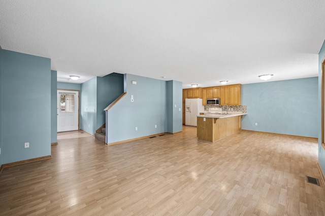 1011 6th Ave NE, Buffalo, MN 55313 - kitchen with white fridge with ice dispenser, stainless steel microwave, light wood-type flooring, a peninsula, and light countertops
