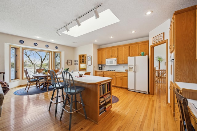 1181 12th Ave NW, New Brighton, MN 55112 - kitchen featuring white appliances, a skylight, rail lighting, a kitchen bar, and light wood-type flooring