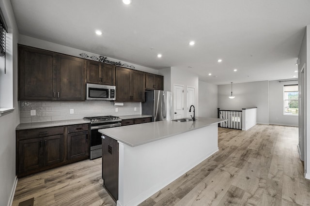 8698 London Cir NE Unit C, Blaine, MN 55449 - kitchen featuring appliances with stainless steel finishes, backsplash, dark brown cabinets, light wood finished floors, and a kitchen island with sink