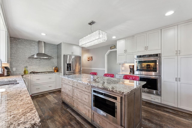8700 Kilbirnie Ter, Brooklyn Park, MN 55443 - kitchen featuring appliances with stainless steel finishes, wall chimney exhaust hood, decorative backsplash, a kitchen island, and dark wood finished floors