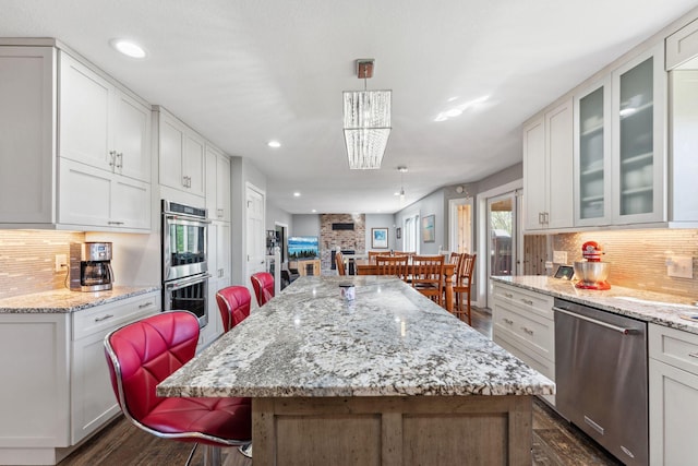 8700 Kilbirnie Ter, Brooklyn Park, MN 55443 - kitchen with appliances with stainless steel finishes, dark wood-style flooring, a kitchen breakfast bar, tasteful backsplash, and white cabinets