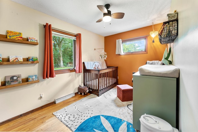 19172 Front Blvd NE, East Bethel, MN 55092 - bedroom featuring a baseboard radiator, wood finished floors, a nursery area, a textured ceiling, and ceiling fan