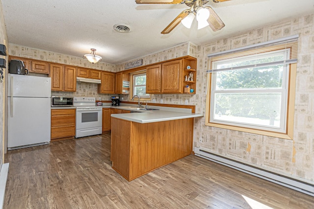 1007 Ruby St NW, Alexandria, MN 56308 - kitchen with white appliances, a baseboard heating unit, brown cabinetry, wallpapered walls, and a peninsula
