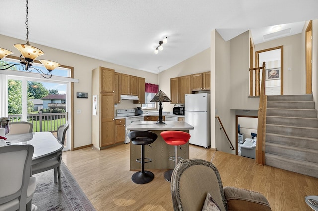 7217 92nd Trl N, Brooklyn Park, MN 55445 - kitchen featuring white appliances, under cabinet range hood, light wood-style flooring, a breakfast bar, and a chandelier
