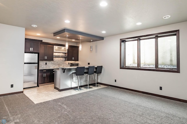 7373 14th St S, Fargo, ND 58104 - kitchen with freestanding refrigerator, light colored carpet, a kitchen bar, dark brown cabinets, and recessed lighting