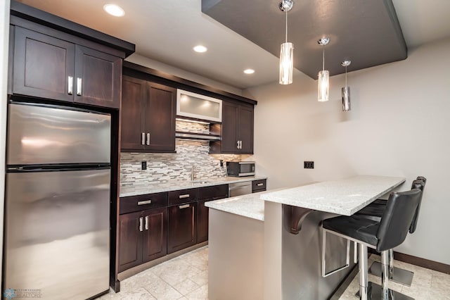 7373 14th St S, Fargo, ND 58104 - kitchen with appliances with stainless steel finishes, decorative backsplash, a peninsula, dark brown cabinets, and a kitchen bar