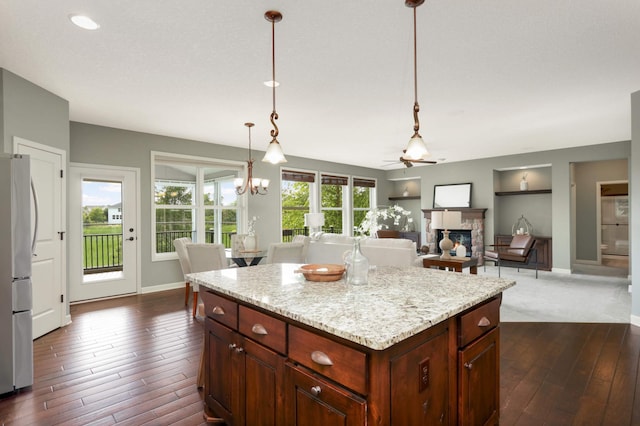 3153 Magnolia Dr, Medina, MN 55340 - kitchen with freestanding refrigerator, a fireplace, dark wood-style flooring, hanging light fixtures, and light stone countertops