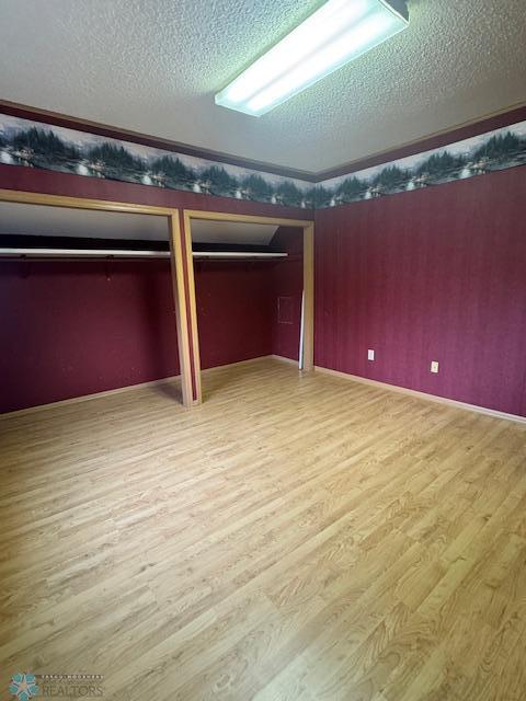 214 7th St, Hatton, ND 58240 - unfurnished bedroom featuring wood finished floors, a textured ceiling, two closets, and wallpapered walls