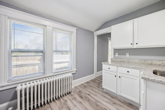 1711 Newton Ave N, Minneapolis, MN 55411 - kitchen featuring radiator heating unit, vaulted ceiling, white cabinets, light wood-style floors, and light stone countertops