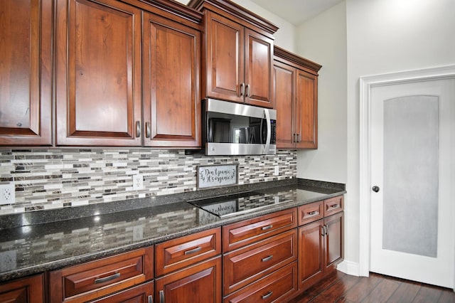1570 Wood Duck Ln NE, Owatonna, MN 55060 - kitchen with stainless steel microwave, black electric cooktop, dark wood finished floors, tasteful backsplash, and dark stone countertops