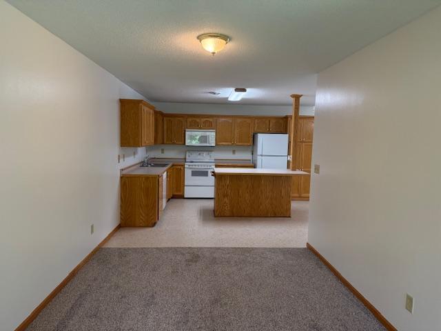 625 Meeker Ct NW, Evansville, MN 56326 - kitchen featuring white appliances, light countertops, light carpet, and brown cabinetry