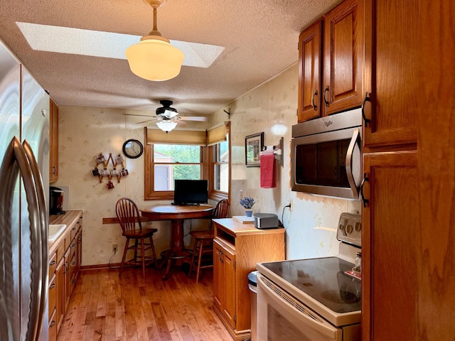 15467 Twilight Rd, Onamia, MN 56359 - kitchen featuring stainless steel appliances, brown cabinetry, light wood-type flooring, a textured ceiling, and a ceiling fan