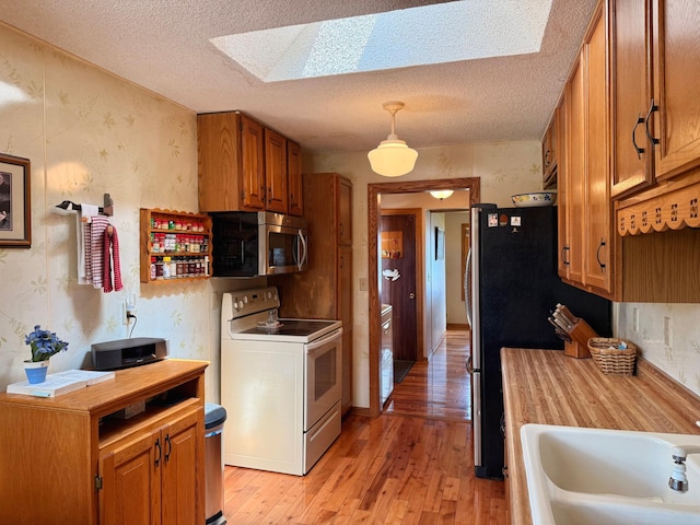 15467 Twilight Rd, Onamia, MN 56359 - kitchen featuring appliances with stainless steel finishes, a skylight, light wood-style floors, brown cabinetry, and wallpapered walls